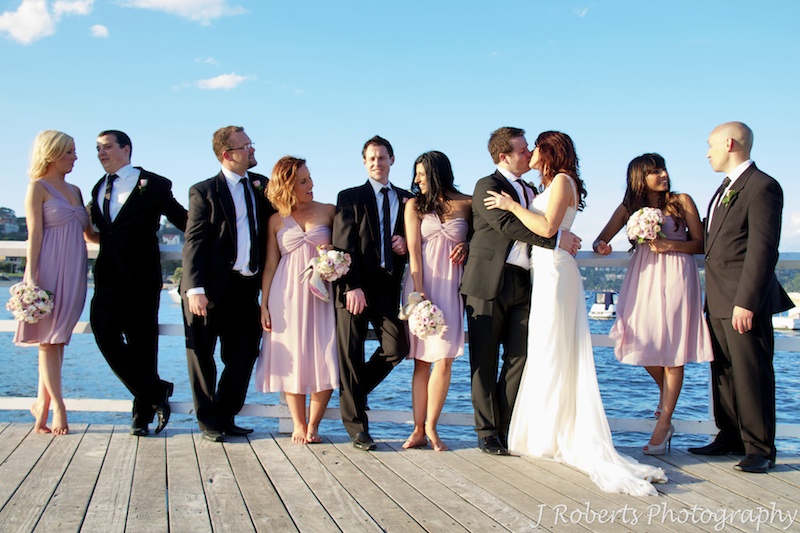 Bridal party chatting in a line with the couple kissing in the middle - wedding photography sydney